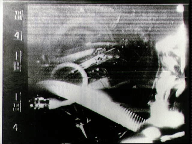 W tle można dostrzec twarz Gordo Coopera, choć bardziej widoczny jest jego hełm. Ujęcie zostało wykonane przez kamerę, która znajdowała się wewnątrz kapsuły "Faith 7".