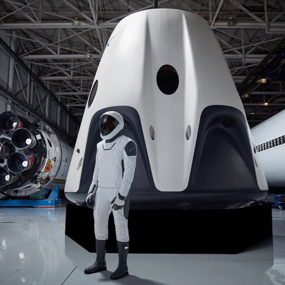 Skafander kosmiczny zaproponowany przez SpaceX, w tle Dragon Crew, czyli załogowa wersja statku.